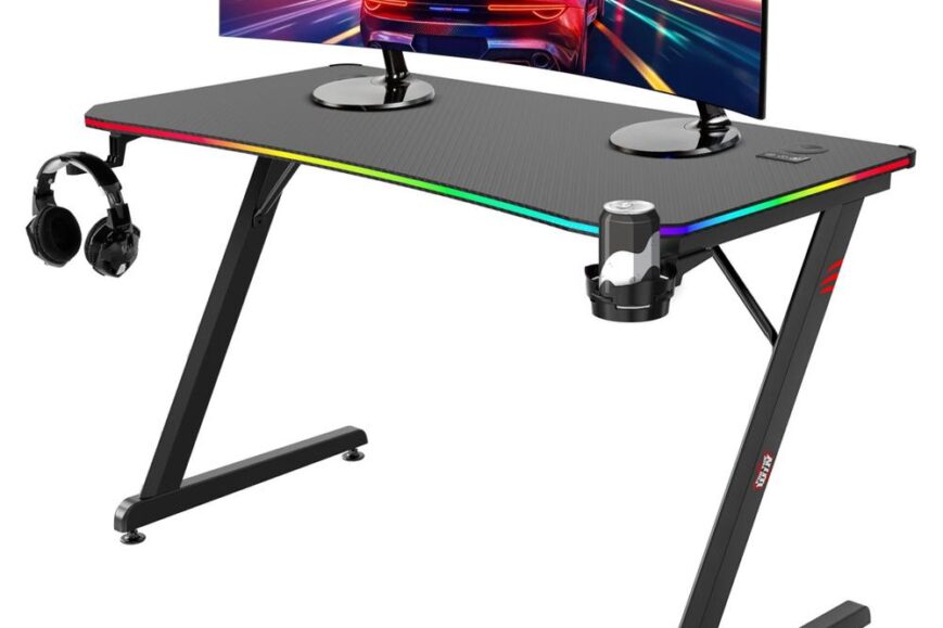 Een moderne gamingtafel met een zwart, gebogen blad en kleurrijke verlichting aan de randen. Op de tafel staan twee monitoren met een racebeeld en er zijn hoofdtelefoons aan de zijkant bevestigd.