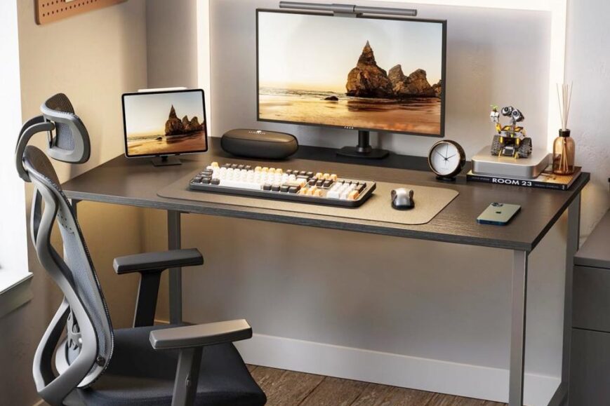 Een stijlvolle bureau-opstelling met een groot computerscherm en een tablet, verlicht door een LED-lamp achter het scherm. De ruimte is verder ingericht met een ergonomische bureaustoel, een toetsenbord, een klok en decoratieve accessoires, wat bijdraagt aan een moderne werk- of speelomgeving.