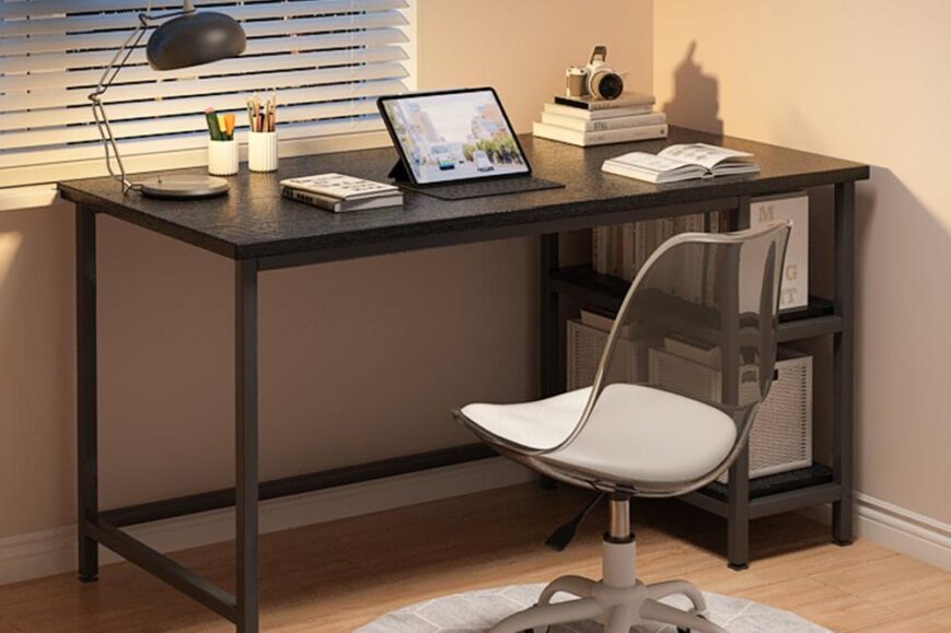 Een moderne werkplek met een zwart bureau, een doorzichtige bureaustoel en een ipad op een standaard. Aan de muur zijn boeken en een camera te zien, met natuurlijk licht dat door de jaloezieën valt.