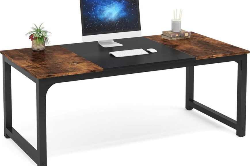 Een modern bureau met een combinatie van een houten en zwart tafelblad, uitgerust met een computer monitor, toetsenbord en muis. Aan de zijkant staat een plant en een paar boeken, wat een stijlvolle werkomgeving creëert.