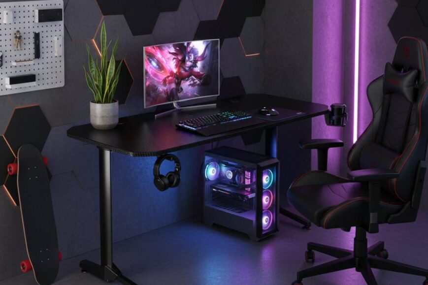 Een modern gamingbureau met een computerscherm, toetsenbord en muis, verlicht door kleurrijke LED-lampen. Naast het bureau staat een comfortabele gamingstoel en een skateboard, met een wanddecoratie van hexagonale panelen op de achtergrond.