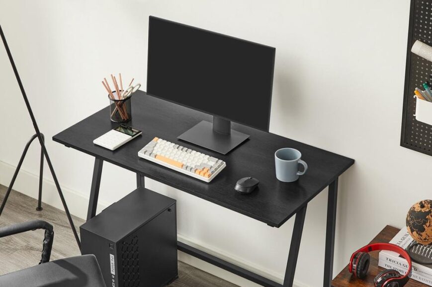 Een moderne bureautafel met een computerscherm, een toetsenbord en een muis, gelegen in een stijlvolle werkomgeving. Daarnaast staan er een plantenpot, een koffiemok en een aantal kantoorbenodigdheden op de tafel, met een computerkast en een stoel naast de tafel.