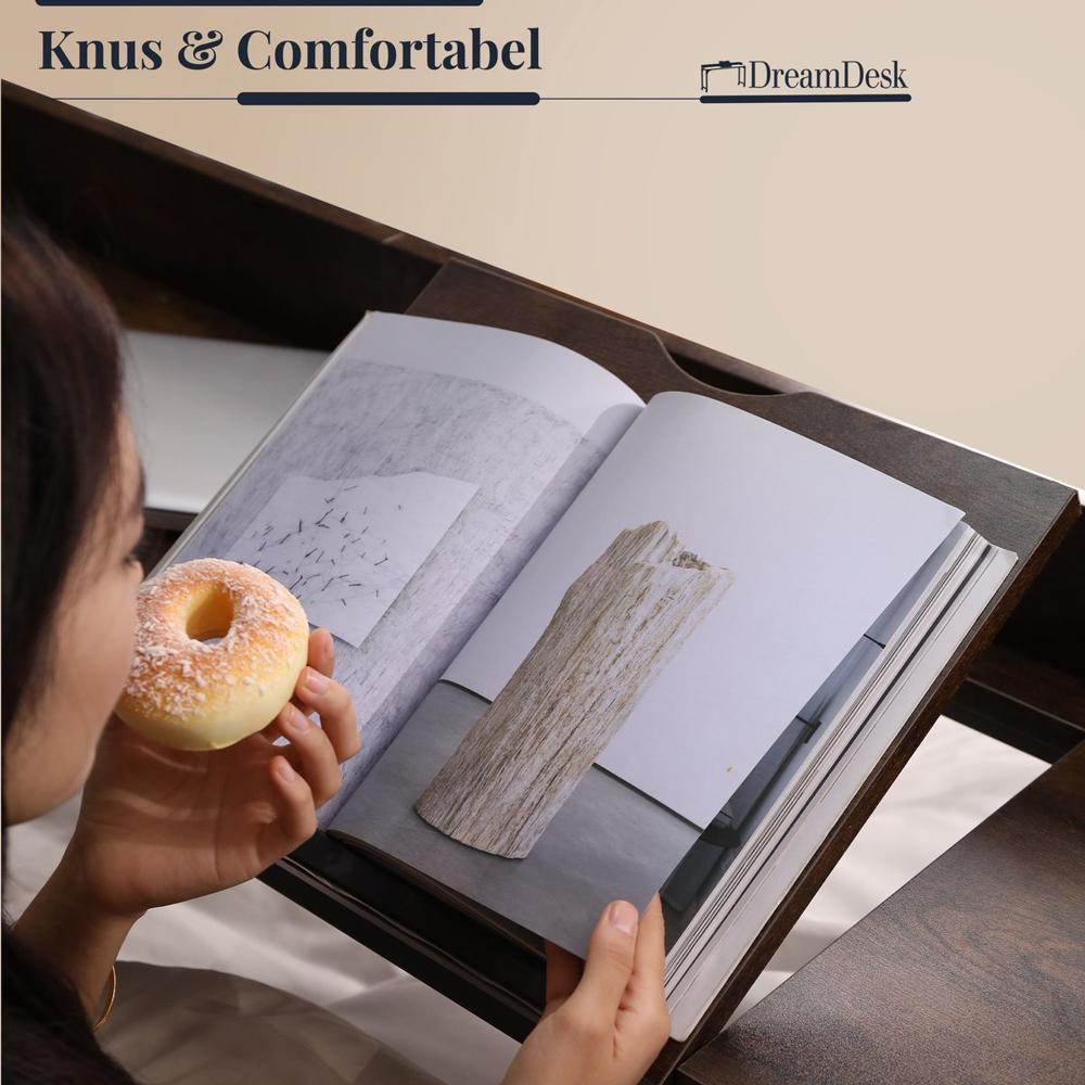 Een persoon leest een open boek terwijl hij een donut vasthoudt. De pagina's tonen een kunstwerk van een houten structuur en een abstracte afbeelding op een muur.