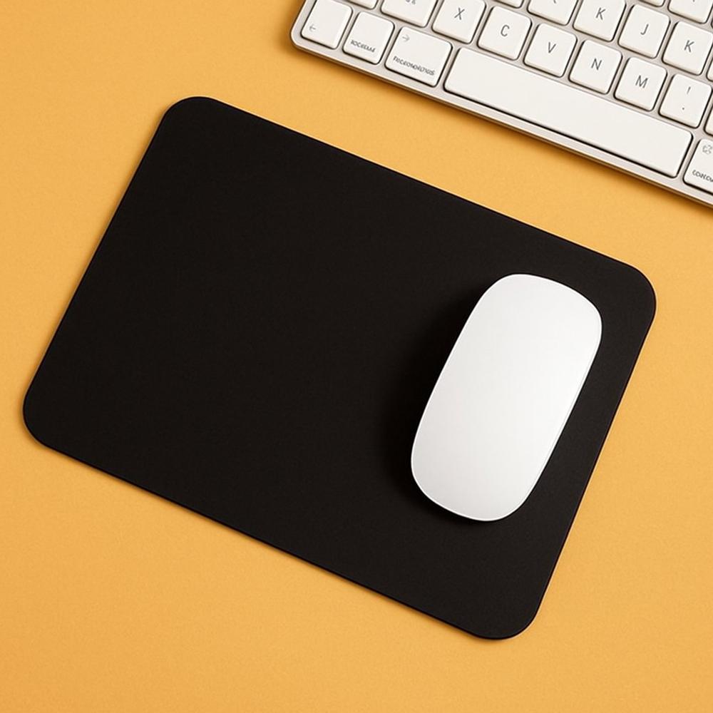 Zwart muismat met een witte muis erop, geplaatst op een achtergrond van warme gele kleur. Op de achtergrond is een toetsenbord zichtbaar, wat de setting van een werkplek benadrukt.